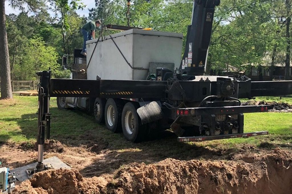 Crane truck lowering a new septic tank into an excavated hole